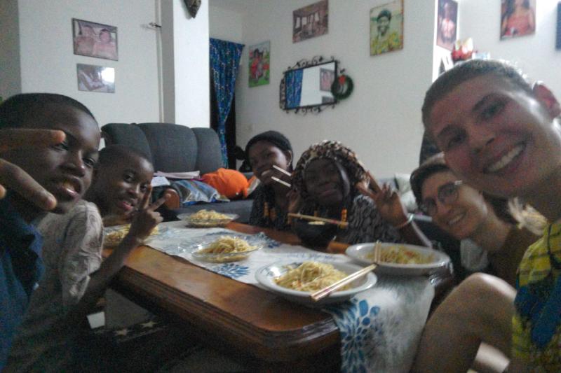 Gruppe von Menschen um einen Tiach sitzend; Asia Nudeln mit Stäbchen in Tellern aauf einem niedrigen Holztisch.